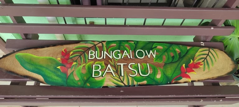 Surfboard-shaped sign for Bungalow Batsu with tropical flowers and green foliage design