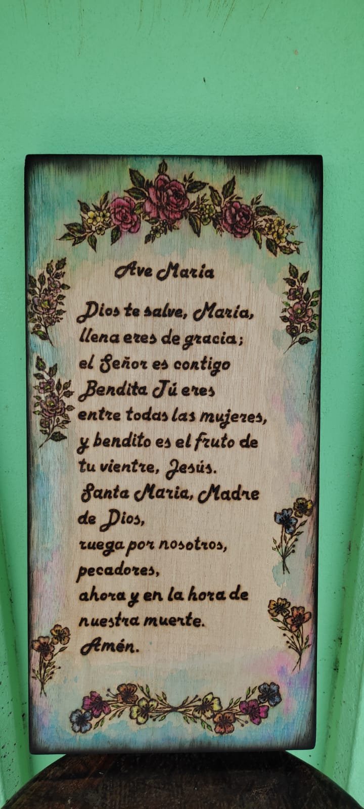 Wooden plaque with Spanish prayer to Mary decorated with burgundy flowers and botanical designs on mint green background