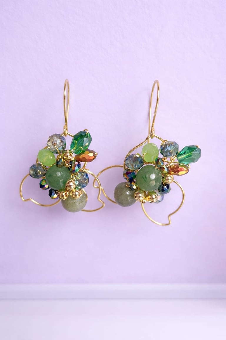 Pair of gold wire earrings with green and gray beads on lavender background