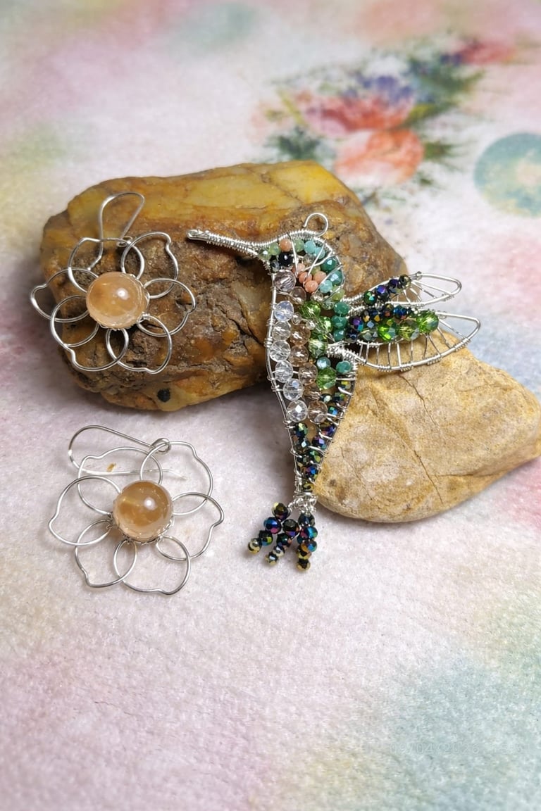 Handmade wire and beaded jewelry pieces including flower brooches and a decorative dragonfly brooch displayed on stones