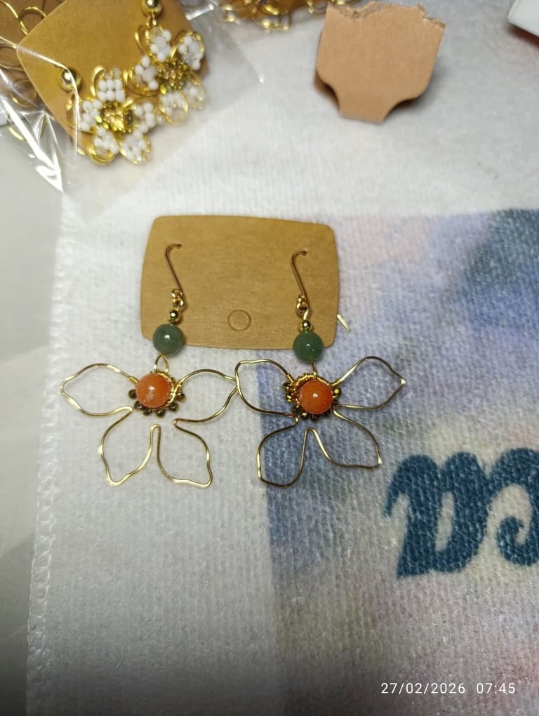 Two pairs of handmade floral earrings displayed on kraft card with beads, on white fabric background
