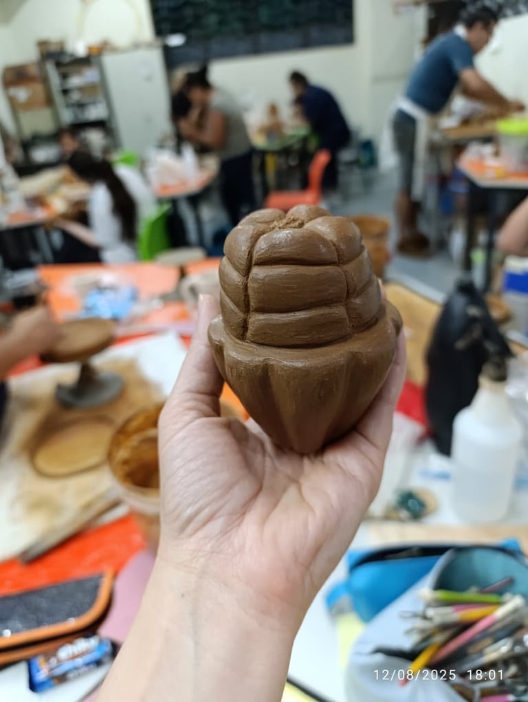 Hand holding a clay sculptured head with layered details in an art classroom workshop setting