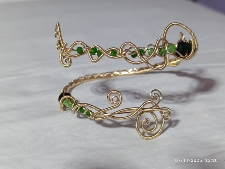 Two ornate gold wire-wrapped bracelets with green beads and black gemstones on white marble surface