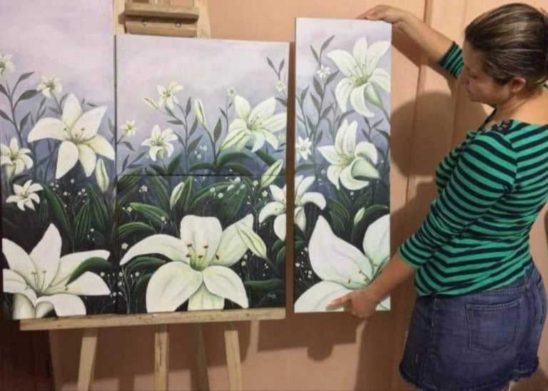Person in green striped shirt viewing three paintings of white flowers with green leaves displayed on an easel