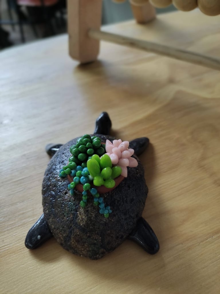 Dark decorative turtle figurine with colorful succulent plants arranged on its back, displayed on a wooden surface