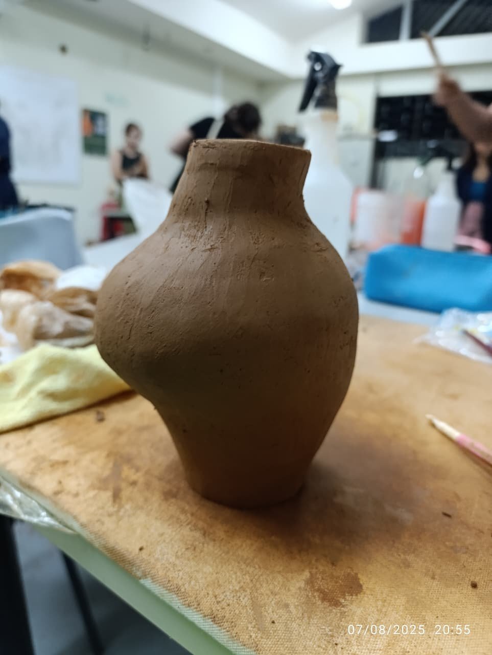 Hand-built clay pottery vessel with rounded bulbous body and narrow neck on wooden work surface in art studio