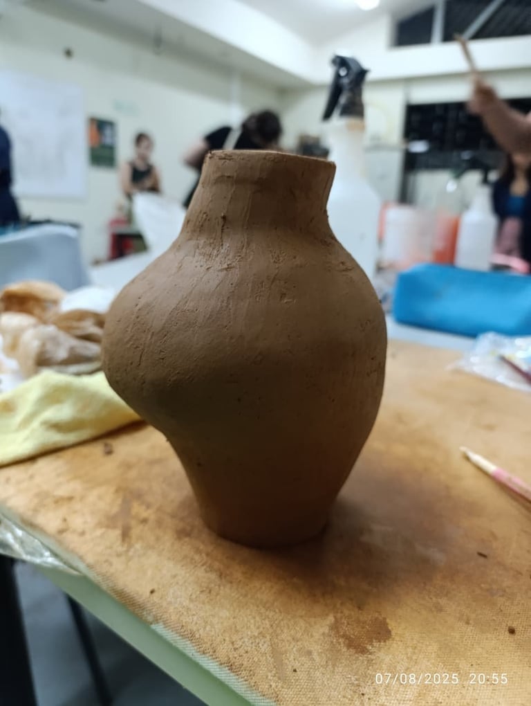 Hand-built clay pottery vessel with rounded bulbous body and narrow neck on wooden work surface in art studio